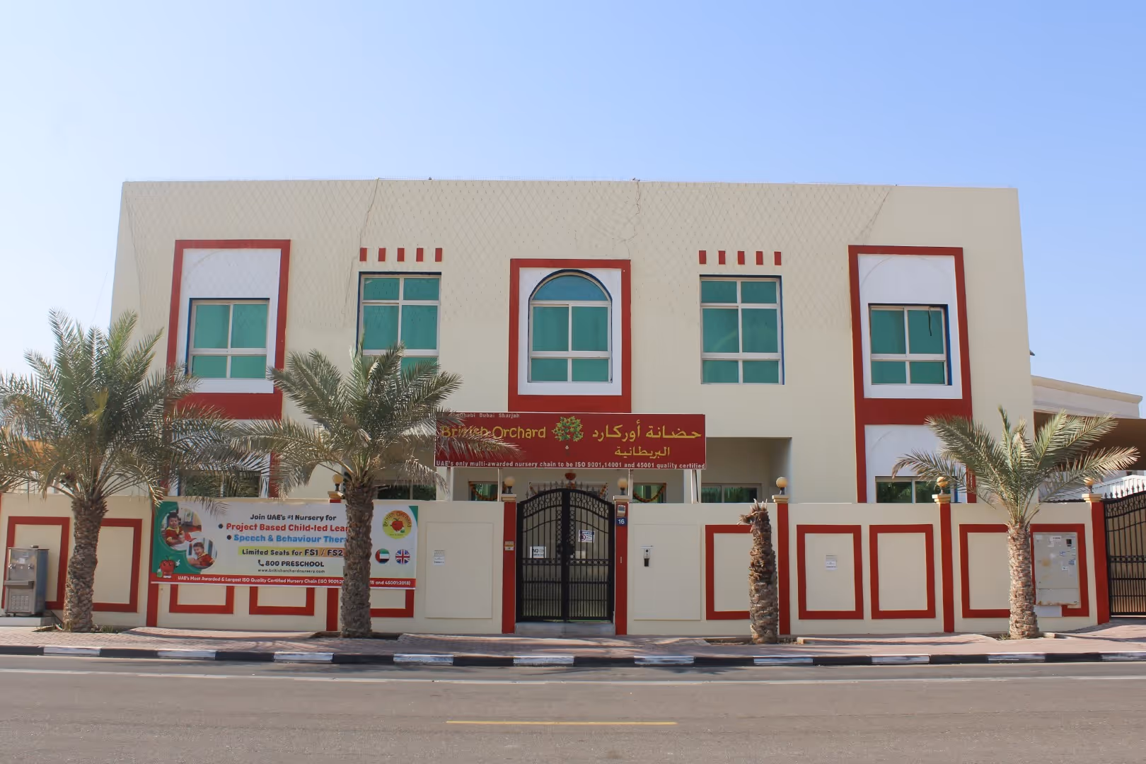 Exterior view of British Orchard Nursery building with palm trees and signage under a clear sky.
