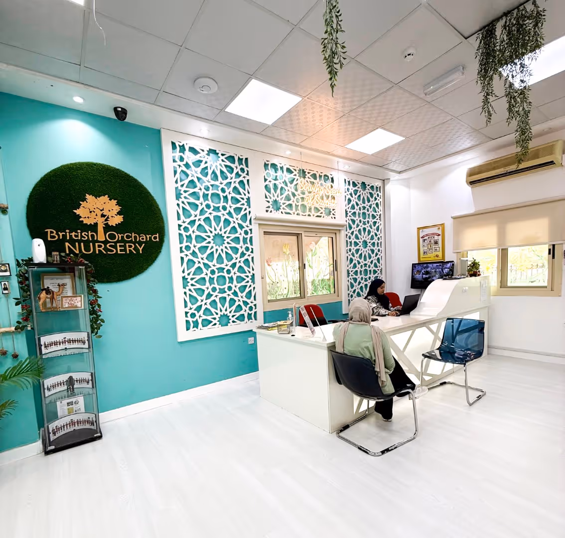 Reception area of British Orchard Nursery with a woman sitting at a white desk and another person seated on a chair facing her, turquoise walls, and decorative white lattice panels.