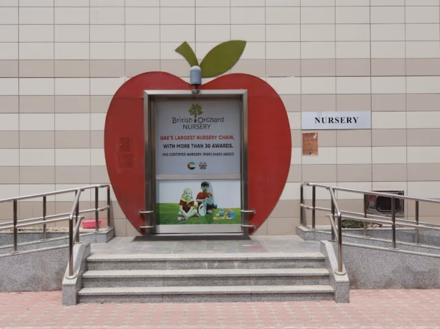 Entrance to British Orchard Nursery shaped like a red apple with two children sitting on grass displayed on the door.