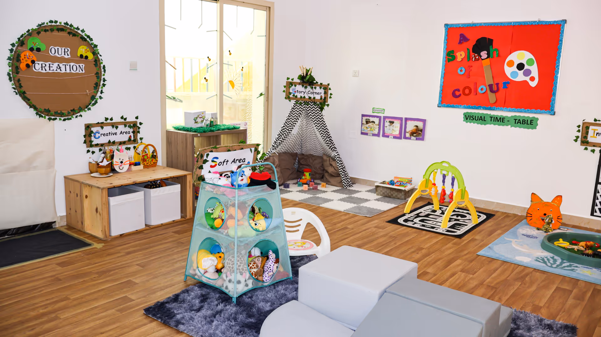 Bright children's playroom with labeled areas including 'Creative Area,' 'Soft Area,' and 'Story Corner' with toys and colorful wall decorations.