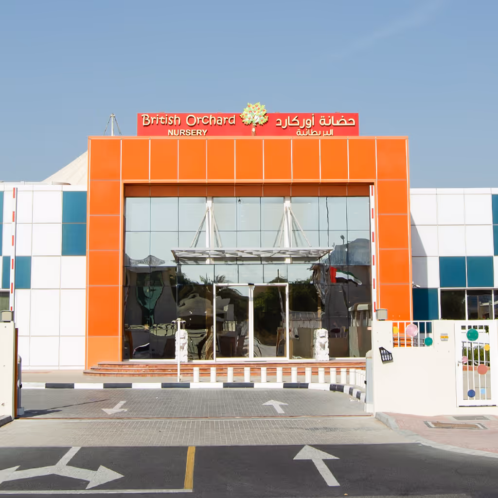 Entrance of British Orchard Nursery with bright orange facade and glass doors under a clear blue sky.