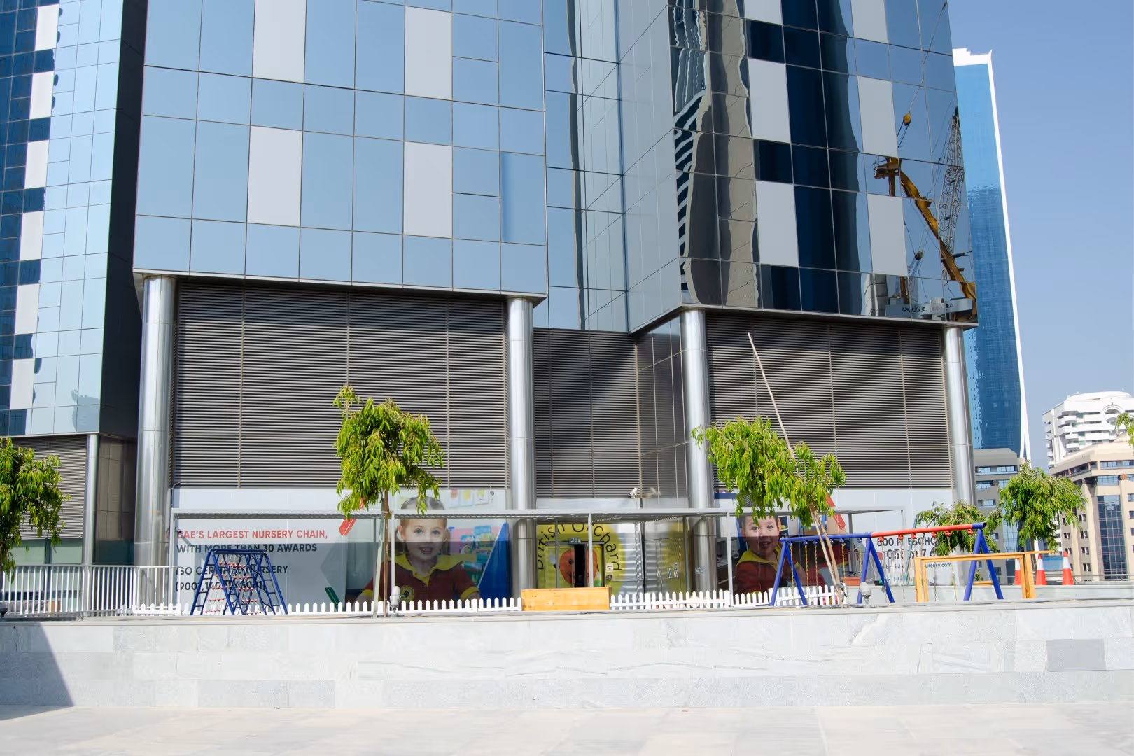 Outdoor children's play area with swings and climbing frames in front of a modern glass building.