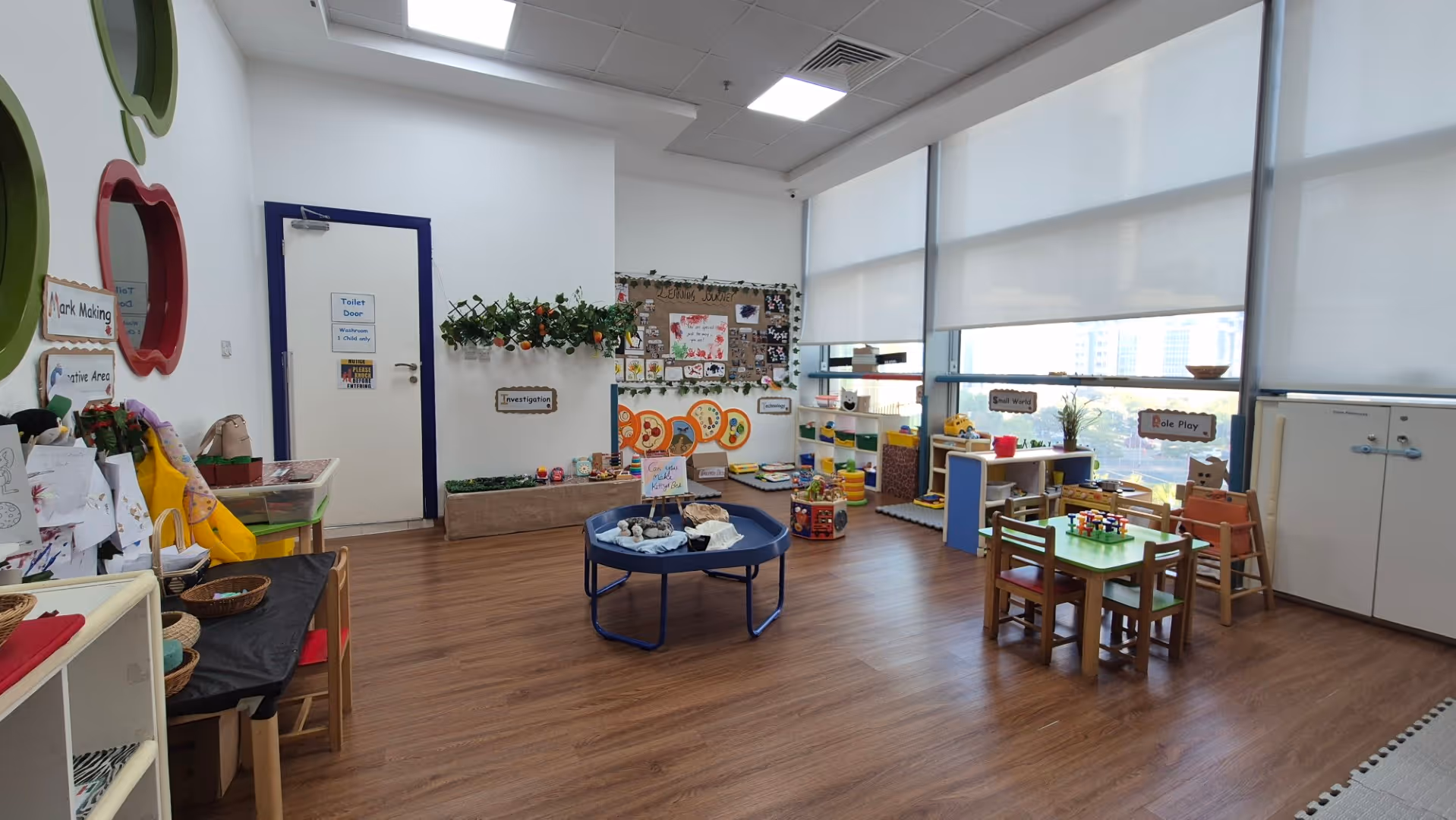 Bright and organized children's playroom with activity tables, educational toys, and labeled learning areas.