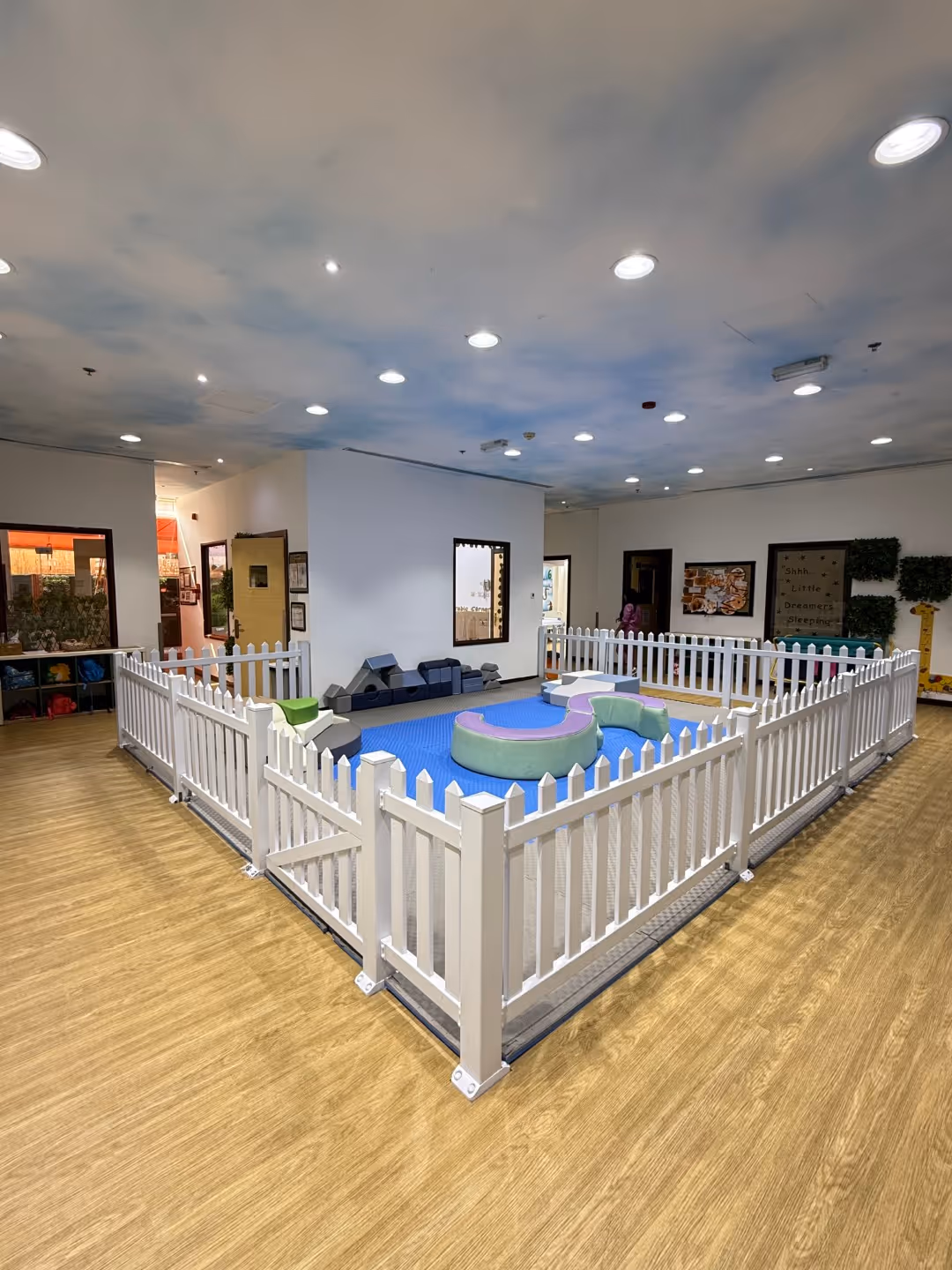 Indoor children's play area enclosed by a white picket fence with soft play cushions inside.