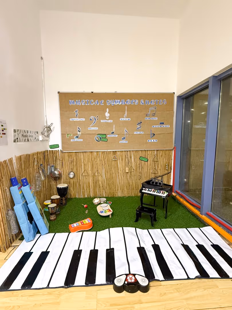 Children's music area with a large piano keyboard mat, small musical instruments, a toy piano, and a musical symbols and notes chart on the wall.
