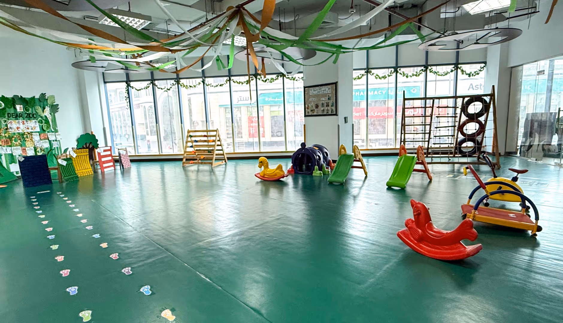 Indoor children's play area with slides, climbing structures, rocking toys, and colorful floor markings.