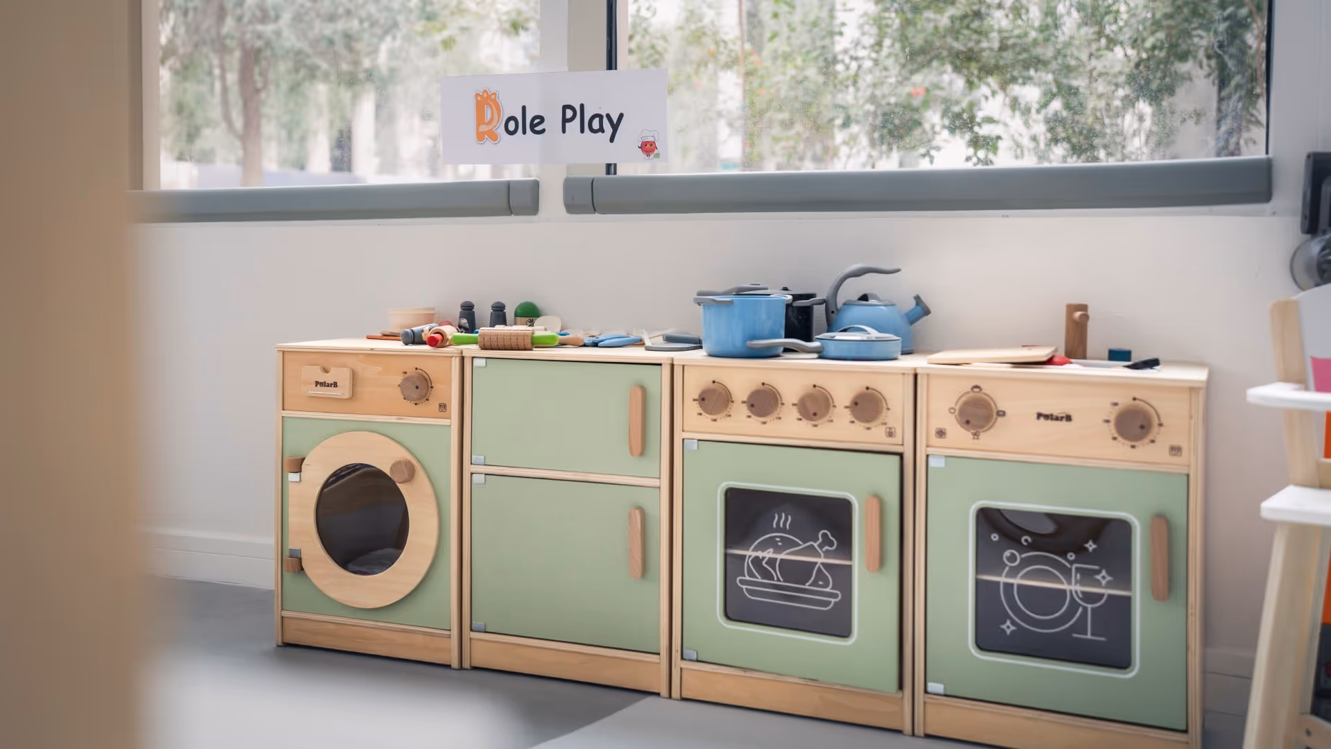 Children's wooden play kitchen set with toy pots, pans, and utensils under a sign that says Role Play.