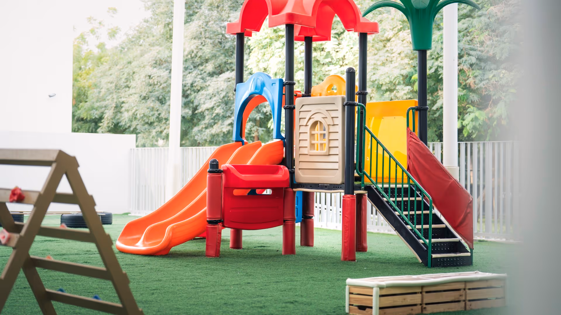 Colorful children's playground with slides, climbing steps, and artificial turf surface outdoors.